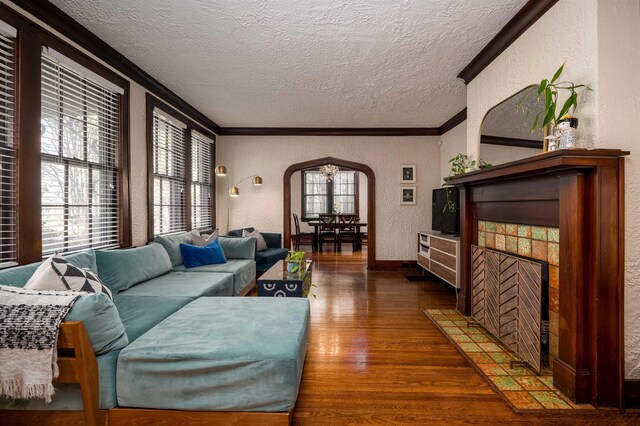 living room with arched walkways, ornamental molding, a textured wall, and wood finished floors