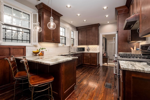 kitchen with a peninsula, stainless steel appliances, tasteful backsplash, under cabinet range hood, and light stone counters