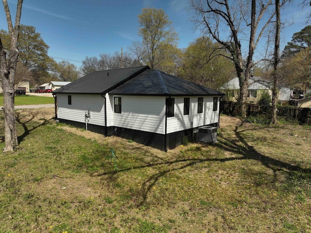 view of side of property with fence, central AC, a yard, and metal roof