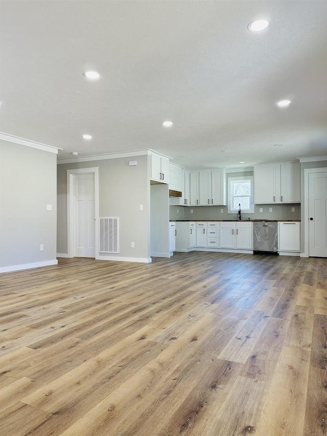 unfurnished living room with crown molding, a sink, light wood finished floors, baseboards, and visible vents