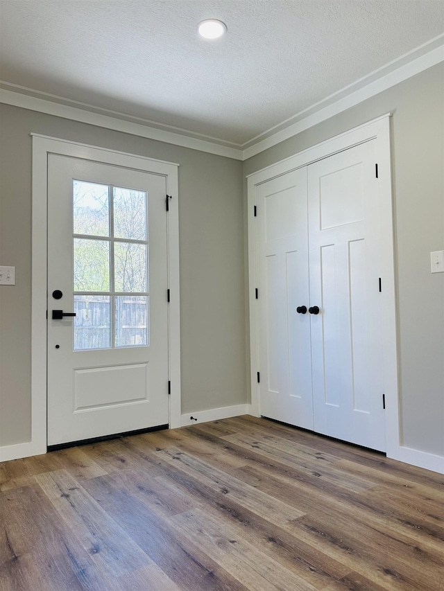 doorway featuring baseboards, a textured ceiling, ornamental molding, and wood finished floors