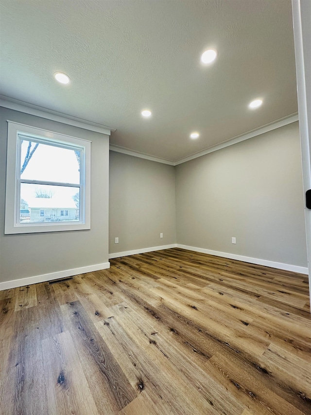 unfurnished room featuring baseboards, visible vents, wood finished floors, and ornamental molding