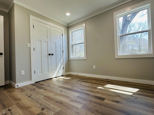 unfurnished bedroom featuring baseboards, a closet, wood finished floors, and ornamental molding