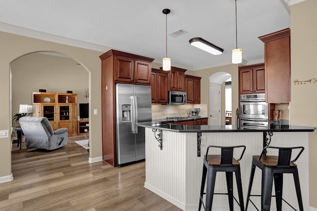 kitchen featuring visible vents, a peninsula, stainless steel appliances, arched walkways, and light wood-style floors