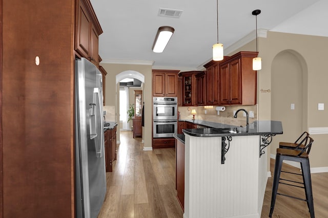 kitchen with a kitchen breakfast bar, stainless steel appliances, arched walkways, visible vents, and a peninsula
