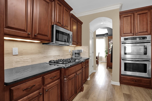 kitchen featuring crown molding, stainless steel appliances, decorative backsplash, arched walkways, and light wood finished floors