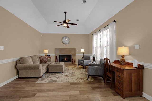 living area with light wood finished floors, baseboards, a warm lit fireplace, and a ceiling fan