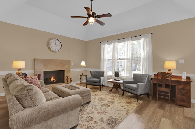 living area featuring light wood finished floors, a premium fireplace, lofted ceiling, baseboards, and ceiling fan