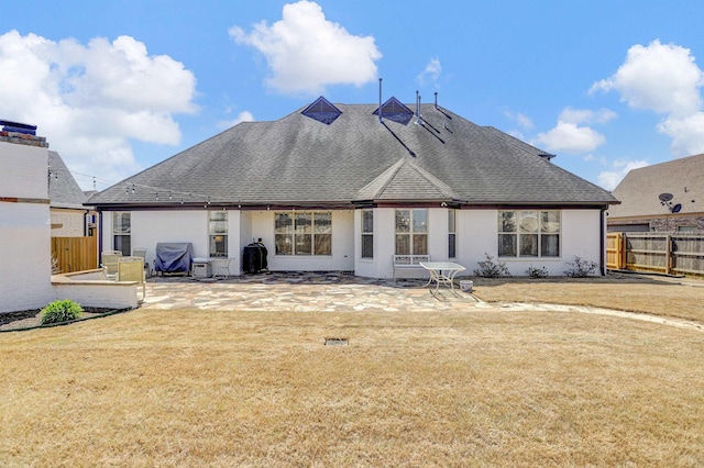 rear view of property featuring a patio, roof with shingles, fence, and a yard