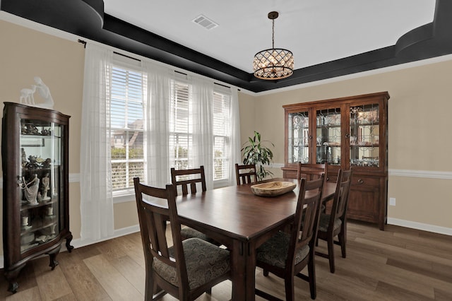 dining space with a tray ceiling, a chandelier, baseboards, visible vents, and light wood-style floors