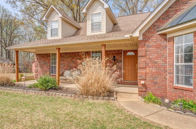 exterior space with a lawn, a porch, brick siding, and roof with shingles