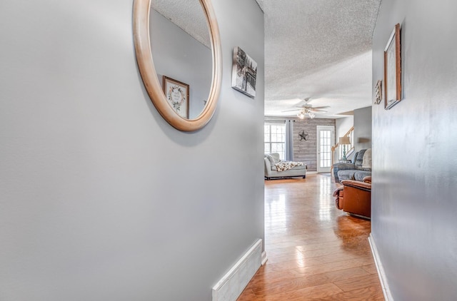 hall featuring light wood finished floors, baseboards, visible vents, and a textured ceiling