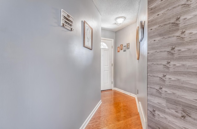 corridor featuring light wood-style floors, baseboards, and a textured ceiling