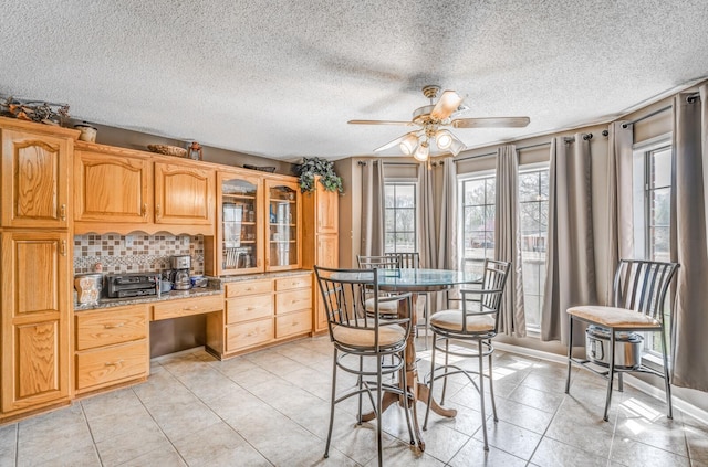 kitchen featuring light tile patterned flooring, tasteful backsplash, glass insert cabinets, built in desk, and ceiling fan
