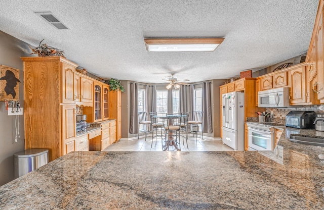 kitchen with tasteful backsplash, white appliances, a sink, stone counters, and visible vents