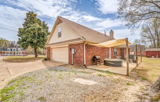 view of side of property with concrete driveway, a patio, brick siding, a garage, and a chimney