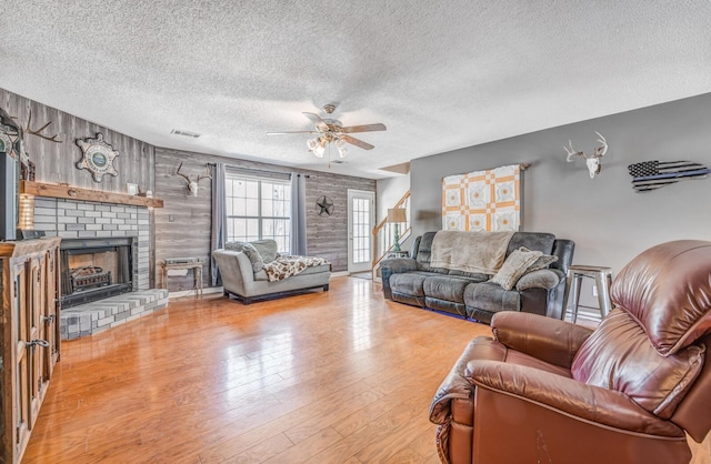 living room with a textured ceiling, a fireplace, a ceiling fan, and wood-type flooring