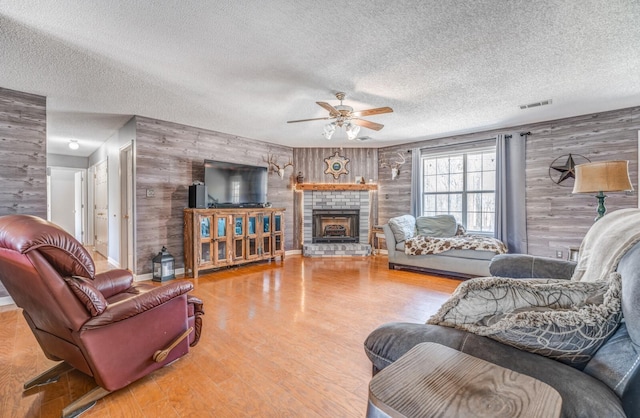 living room featuring a ceiling fan, a fireplace, wooden walls, wood finished floors, and visible vents