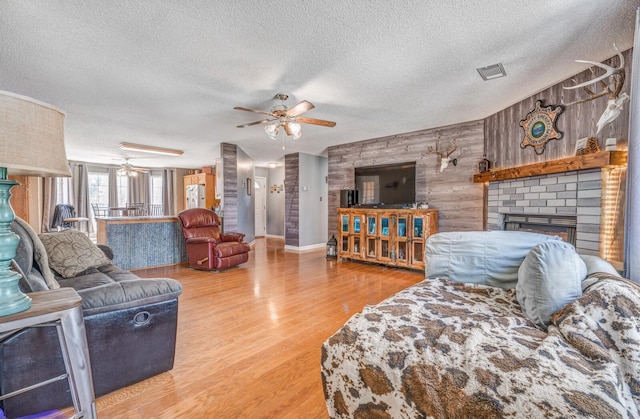 living room with a brick fireplace, wood walls, visible vents, a ceiling fan, and wood finished floors