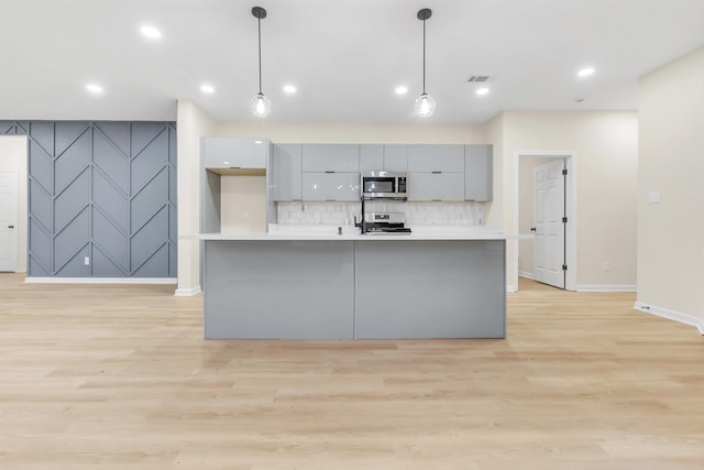kitchen featuring an accent wall, modern cabinets, gray cabinetry, stainless steel appliances, and light wood-style floors