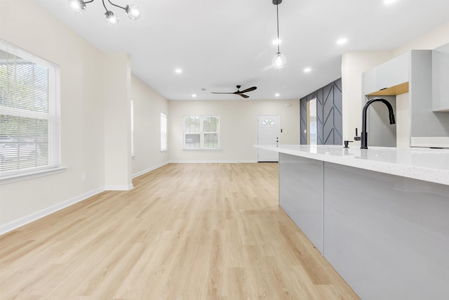 kitchen featuring decorative light fixtures, light wood-type flooring, ceiling fan with notable chandelier, baseboards, and modern cabinets
