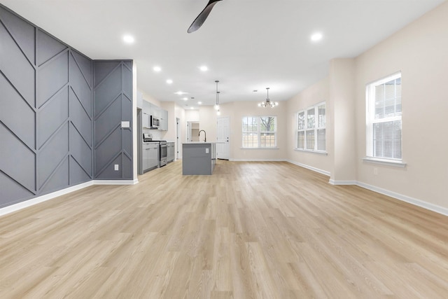 unfurnished living room with a sink, light wood-style flooring, baseboards, ceiling fan with notable chandelier, and recessed lighting