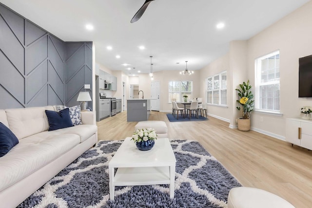 living room with ceiling fan with notable chandelier, baseboards, light wood-style floors, and recessed lighting