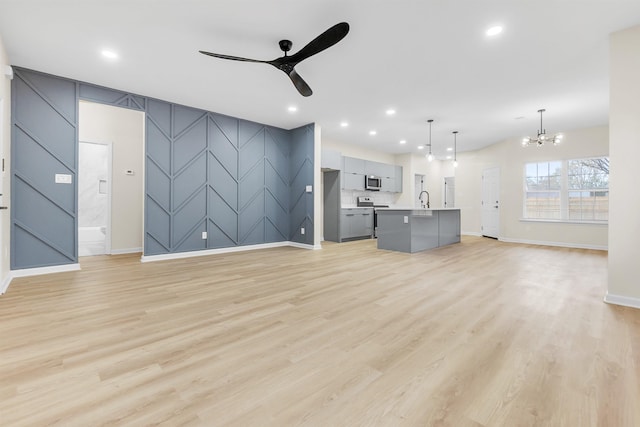 unfurnished living room featuring recessed lighting, ceiling fan with notable chandelier, an accent wall, a sink, and light wood-style flooring