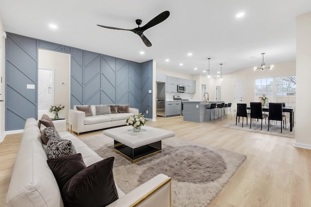living room with light wood-type flooring, an accent wall, recessed lighting, and ceiling fan with notable chandelier