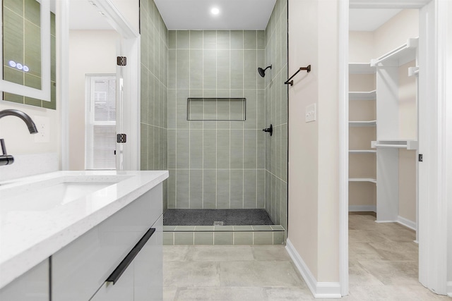 bathroom with a spacious closet, vanity, baseboards, and tiled shower