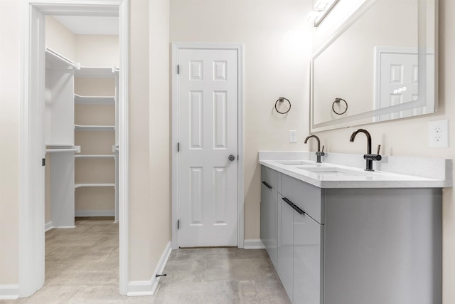 full bath featuring double vanity, a sink, a walk in closet, and baseboards