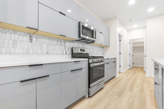 kitchen with backsplash, light wood finished floors, appliances with stainless steel finishes, modern cabinets, and gray cabinetry