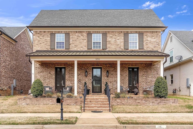 view of front of property featuring covered porch, a standing seam roof, roof with shingles, brick siding, and metal roof