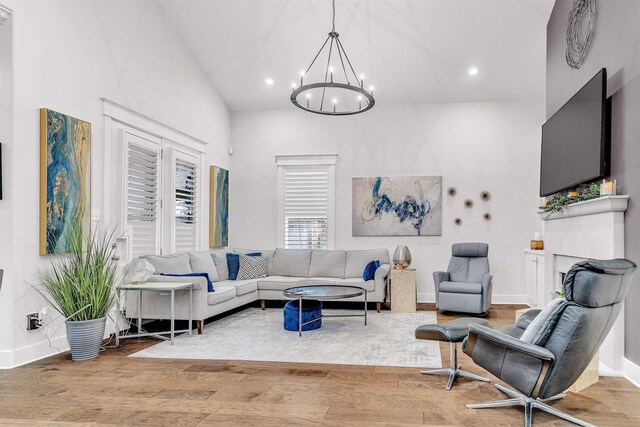 living room with baseboards, wood finished floors, recessed lighting, a high ceiling, and an inviting chandelier