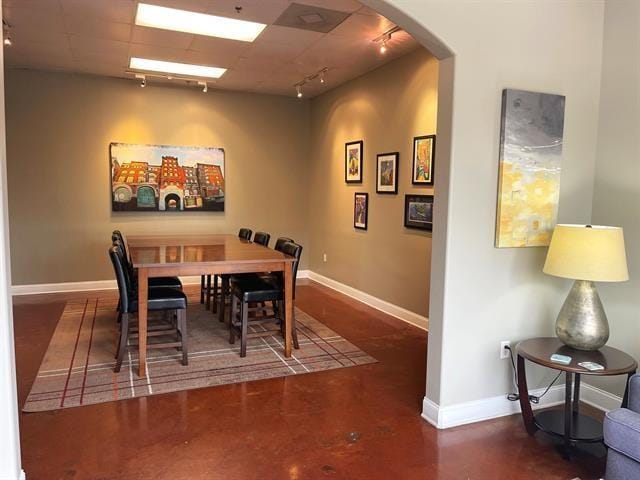 dining room featuring rail lighting, arched walkways, finished concrete flooring, and baseboards
