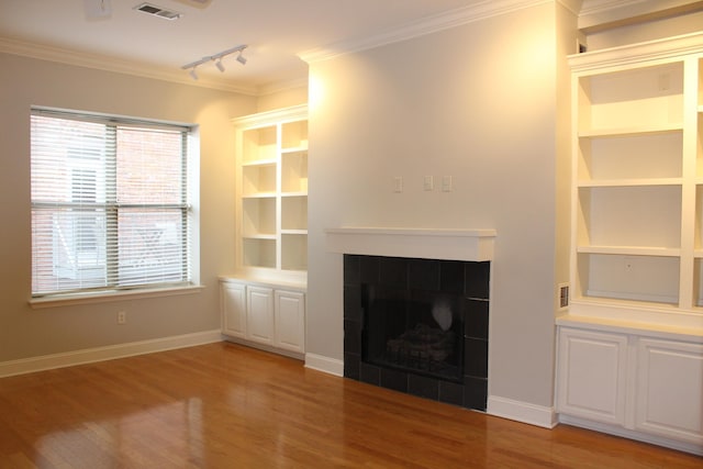 unfurnished living room with crown molding, light wood-style flooring, a fireplace, rail lighting, and visible vents