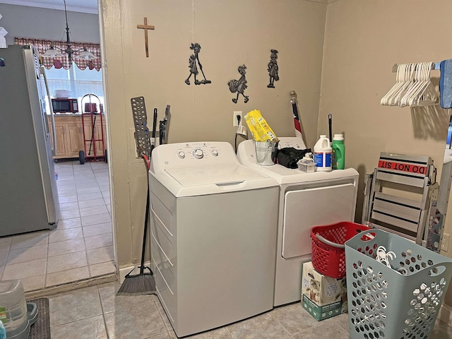 clothes washing area with washing machine and clothes dryer, laundry area, light tile patterned floors, and an inviting chandelier