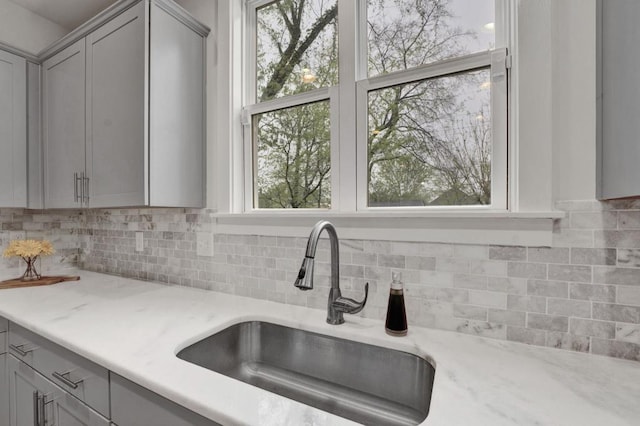 kitchen with gray cabinetry, light stone countertops, decorative backsplash, and a sink