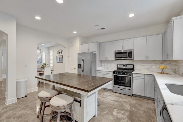 kitchen with decorative backsplash, a breakfast bar, stainless steel appliances, arched walkways, and a center island