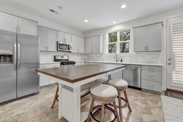 kitchen featuring butcher block countertops, visible vents, a breakfast bar, stainless steel appliances, and backsplash