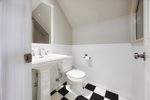 half bathroom with vaulted ceiling, toilet, tile patterned floors, a wainscoted wall, and a sink
