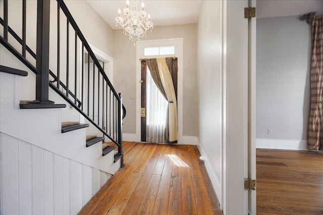 foyer entrance with stairs, a chandelier, baseboards, and wood-type flooring