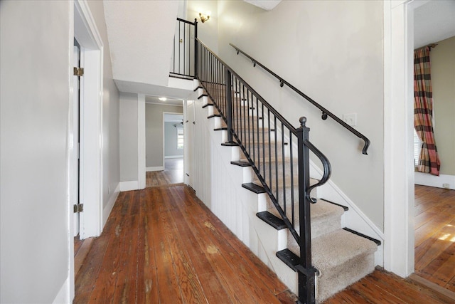 staircase featuring baseboards, a towering ceiling, and wood-type flooring
