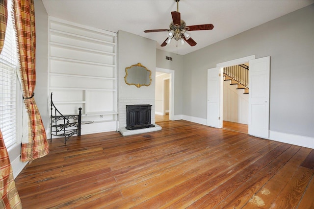 unfurnished living room with hardwood / wood-style flooring, baseboards, stairs, and built in shelves