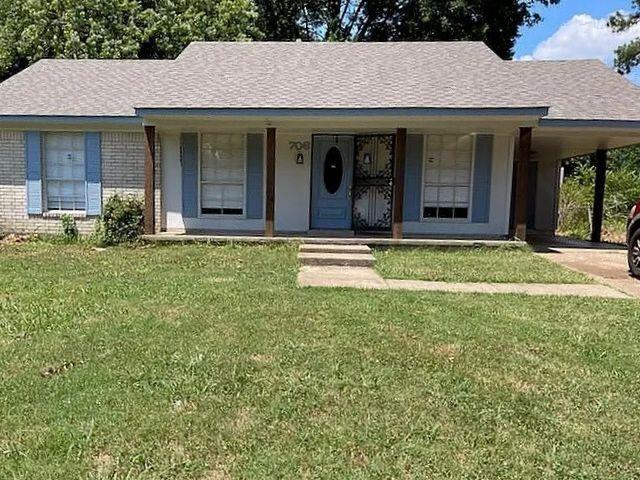 single story home featuring a front yard, covered porch, concrete driveway, brick siding, and a carport