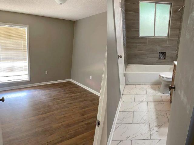 bathroom with toilet, shower / washtub combination, a textured ceiling, marble finish floor, and baseboards