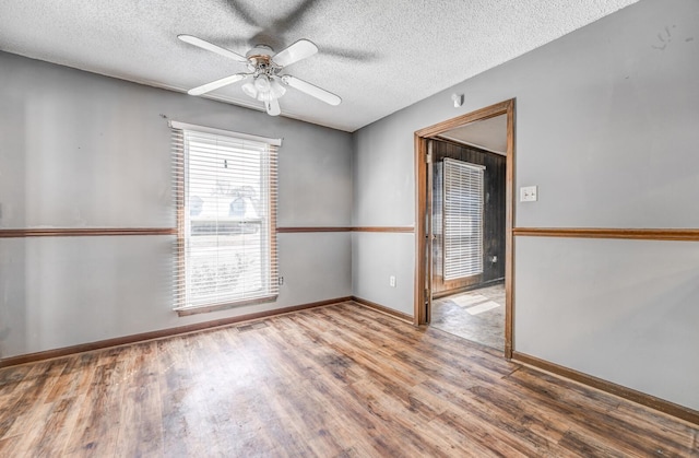 empty room with baseboards, wood finished floors, ceiling fan, and a textured ceiling