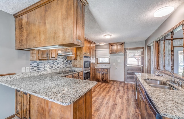 kitchen featuring a sink, appliances with stainless steel finishes, a peninsula, brown cabinets, and under cabinet range hood