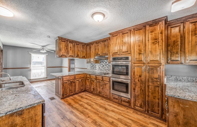 kitchen featuring brown cabinets, a peninsula, a sink, and stainless steel double oven