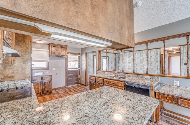 kitchen with a sink, a peninsula, light stone countertops, black appliances, and brown cabinets